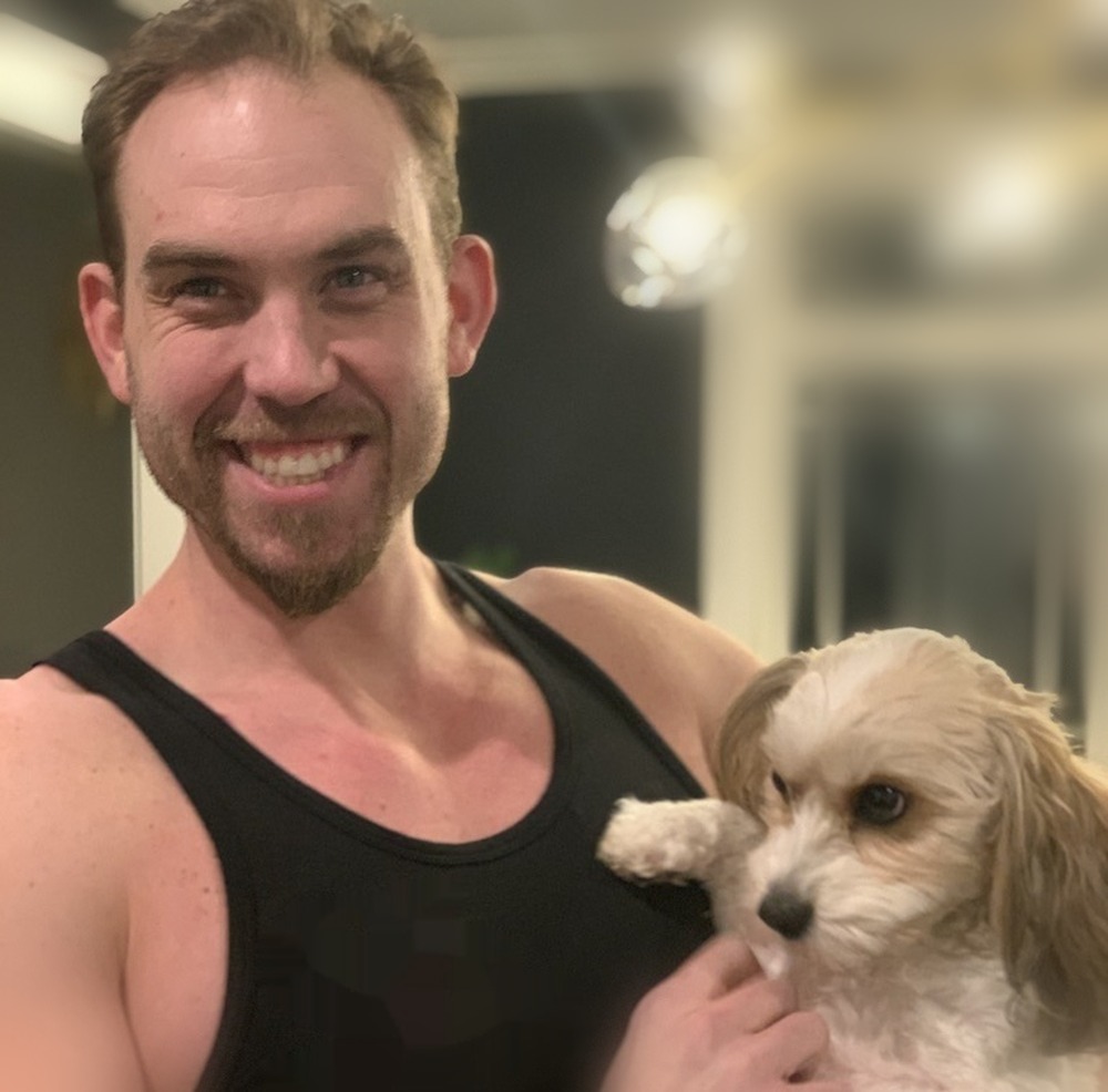 Wes Rogers smiling, holding Goldie, a small cream-and-tan dog he sits for regularly